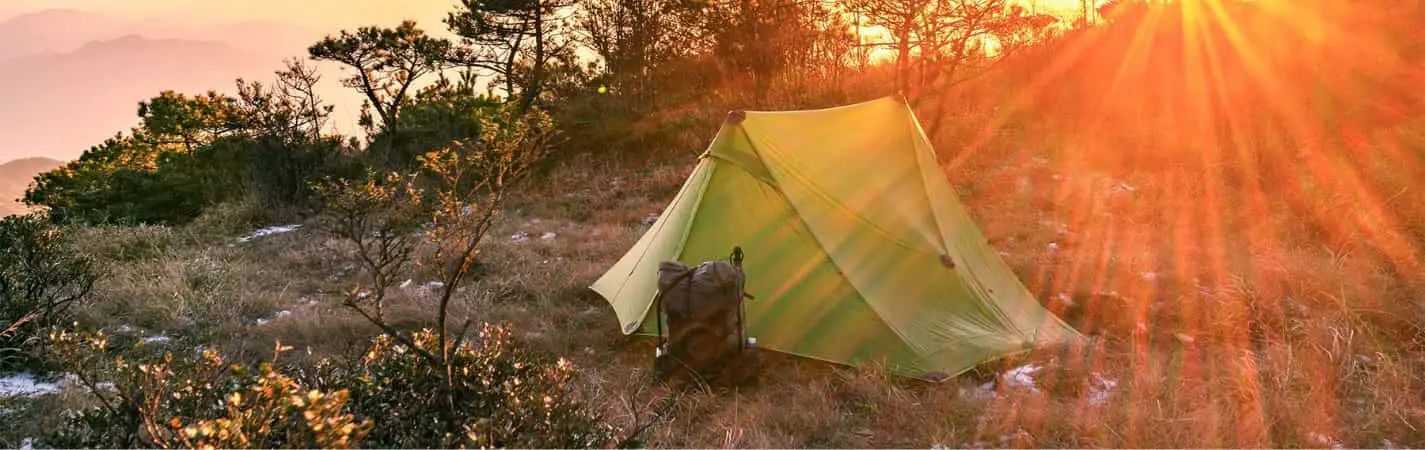 3F UL Lanshan 2P green tent on the grass with a backpoack outside at sunset