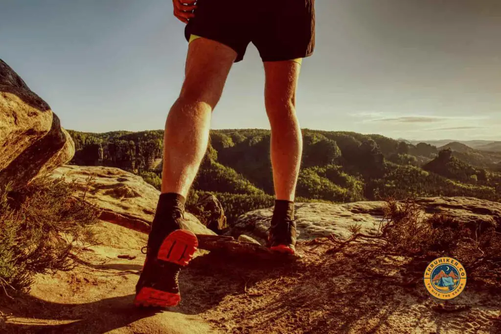 Man standing on top of a peak showing off his trail runners